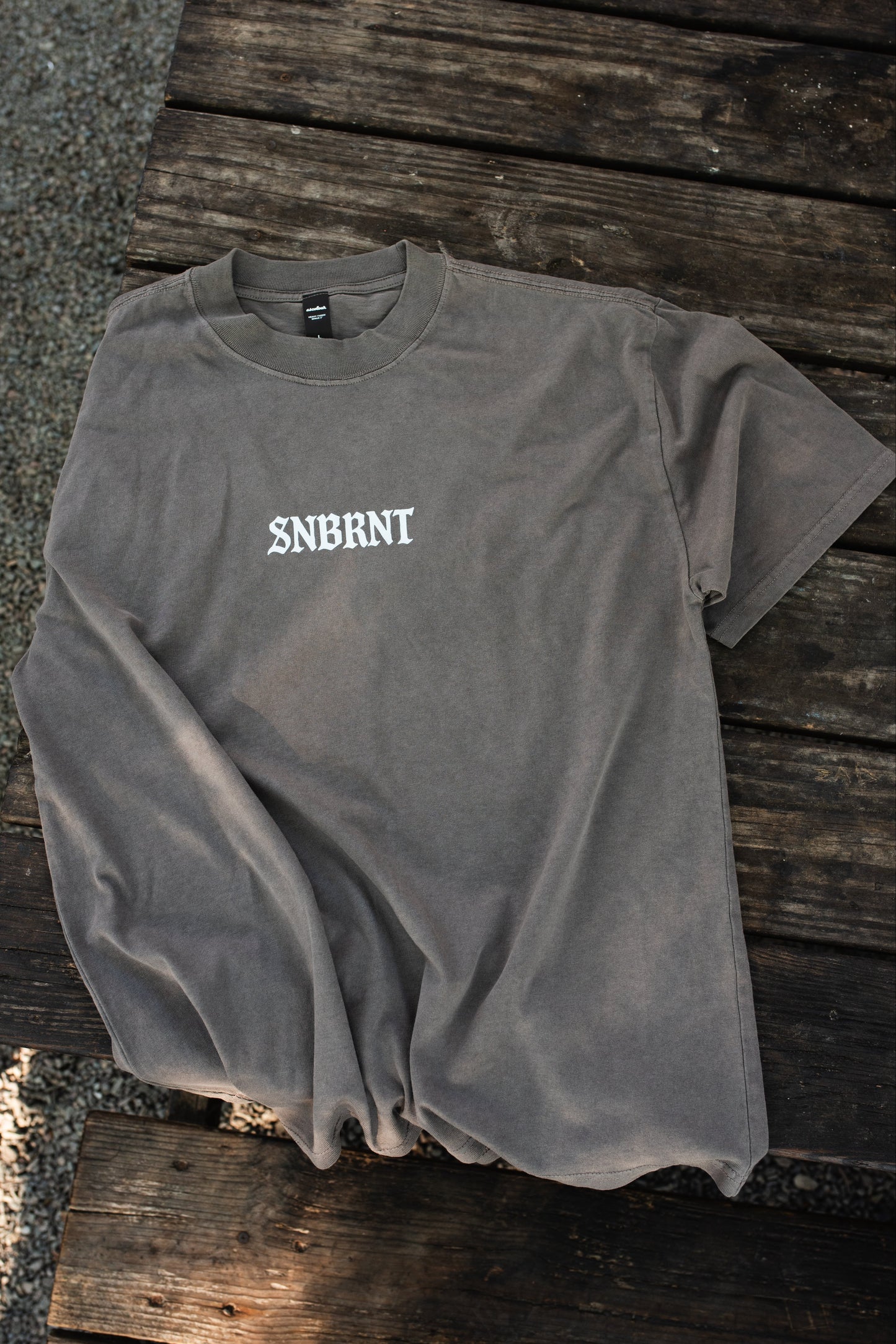 Gray t-shirt with 'SNBRNT' logo on a wooden surface