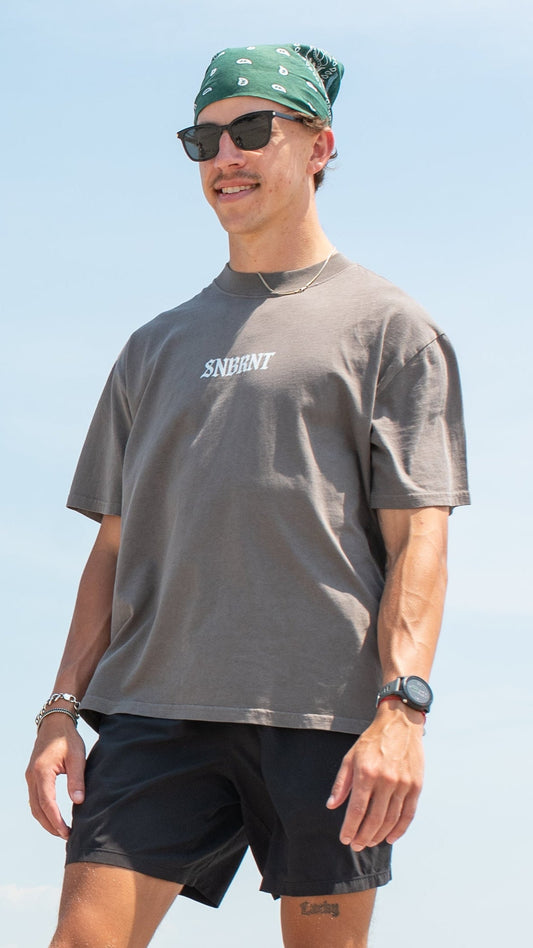 standing on a rock with SURF TEE SHIRT design at the beach. SNBRNT