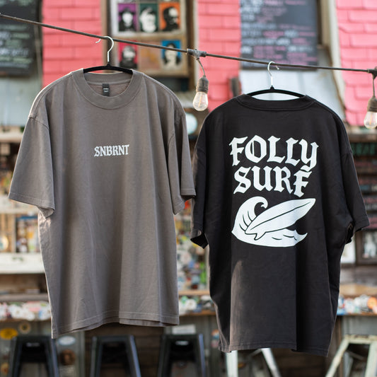 Two t-shirts, one gray and one black with white text, hanging on a clothesline in front of a store with pink walls.