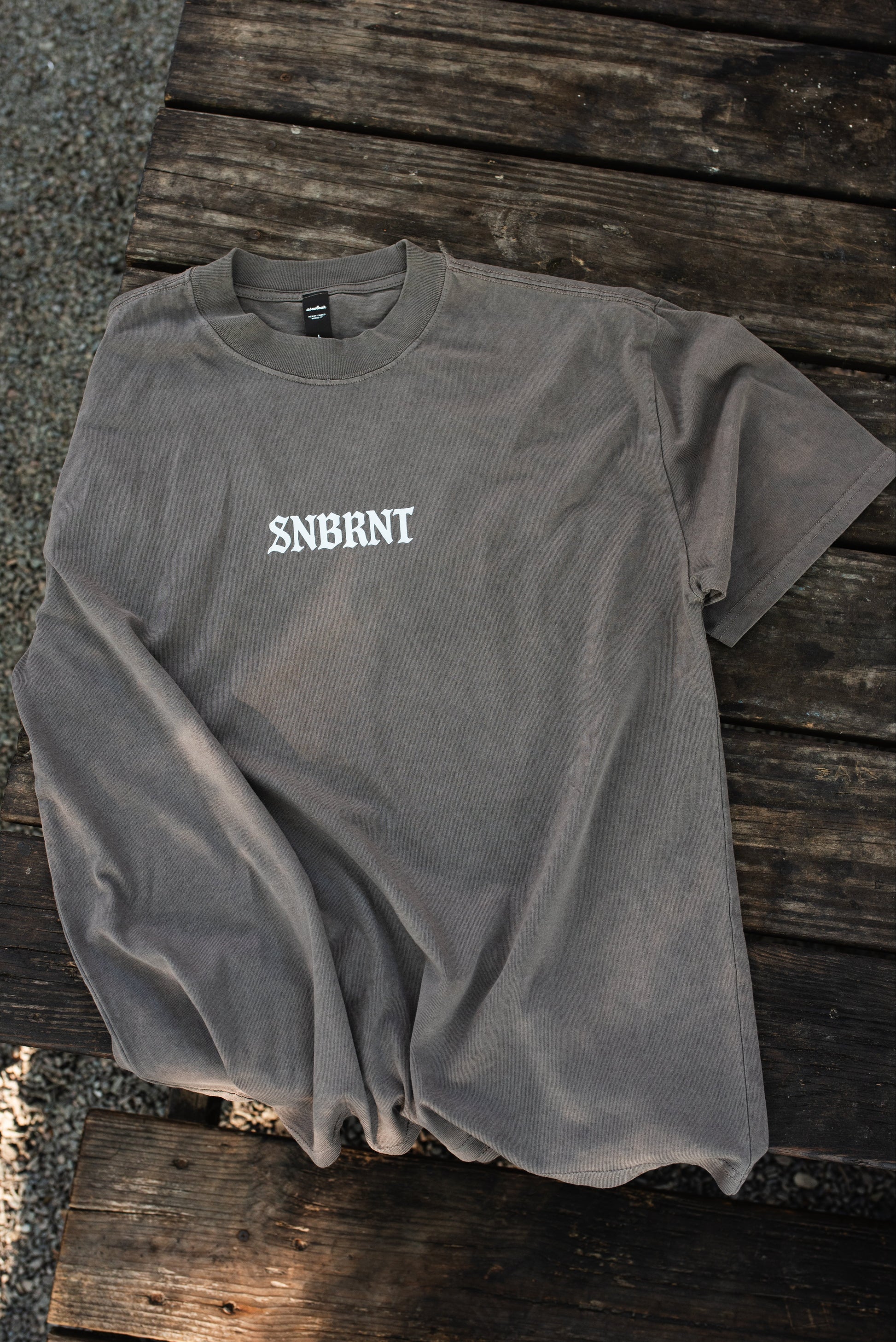 Gray t-shirt with 'SNBRNT' logo on a wooden surface