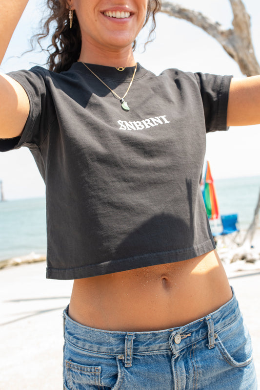 Person wearing a black t-shirt with 'SNBRNT' printed on it at a beach.